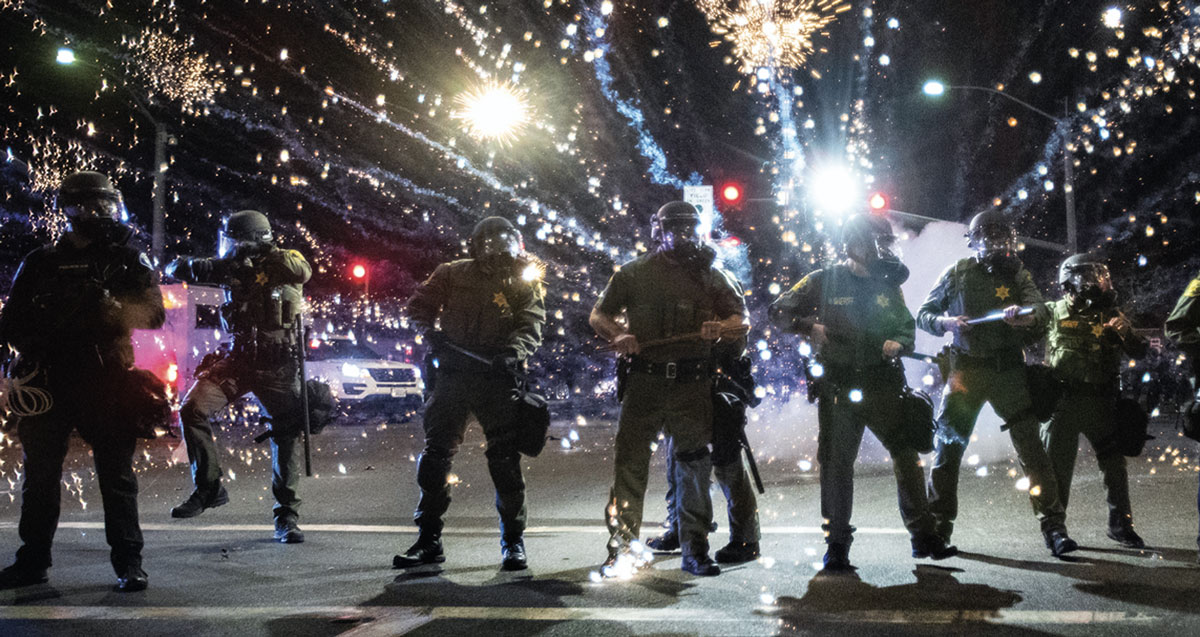 Photo depicting police waring riot gear at a rally with sparks flying