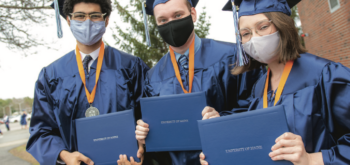 Three members of the graduating class holding up their University of Maine diplomas.