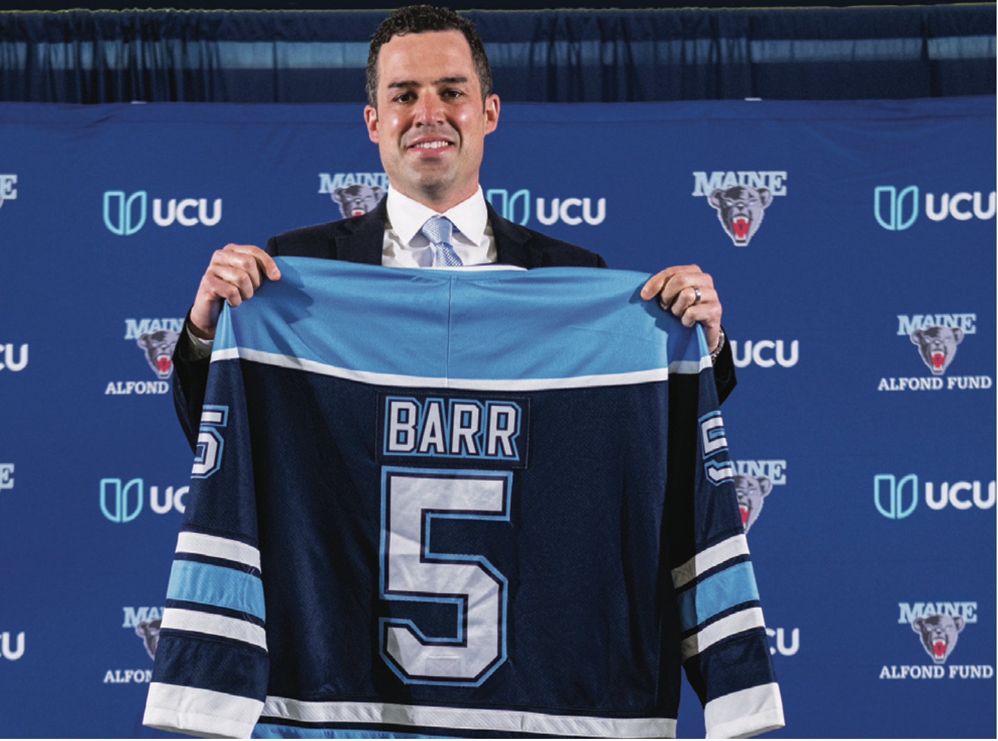 Ben Barr holding up a #5 jersey that reads "BARR" over the number